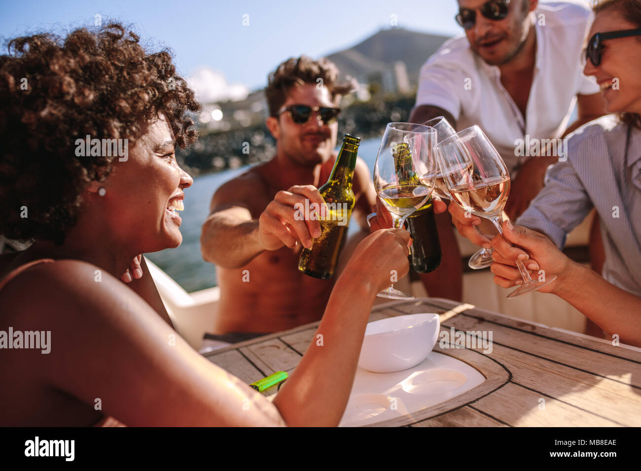Multiracial group of people toasting drinks on boat. Young people enjoying at a boat party and having drinks. Stock Photo