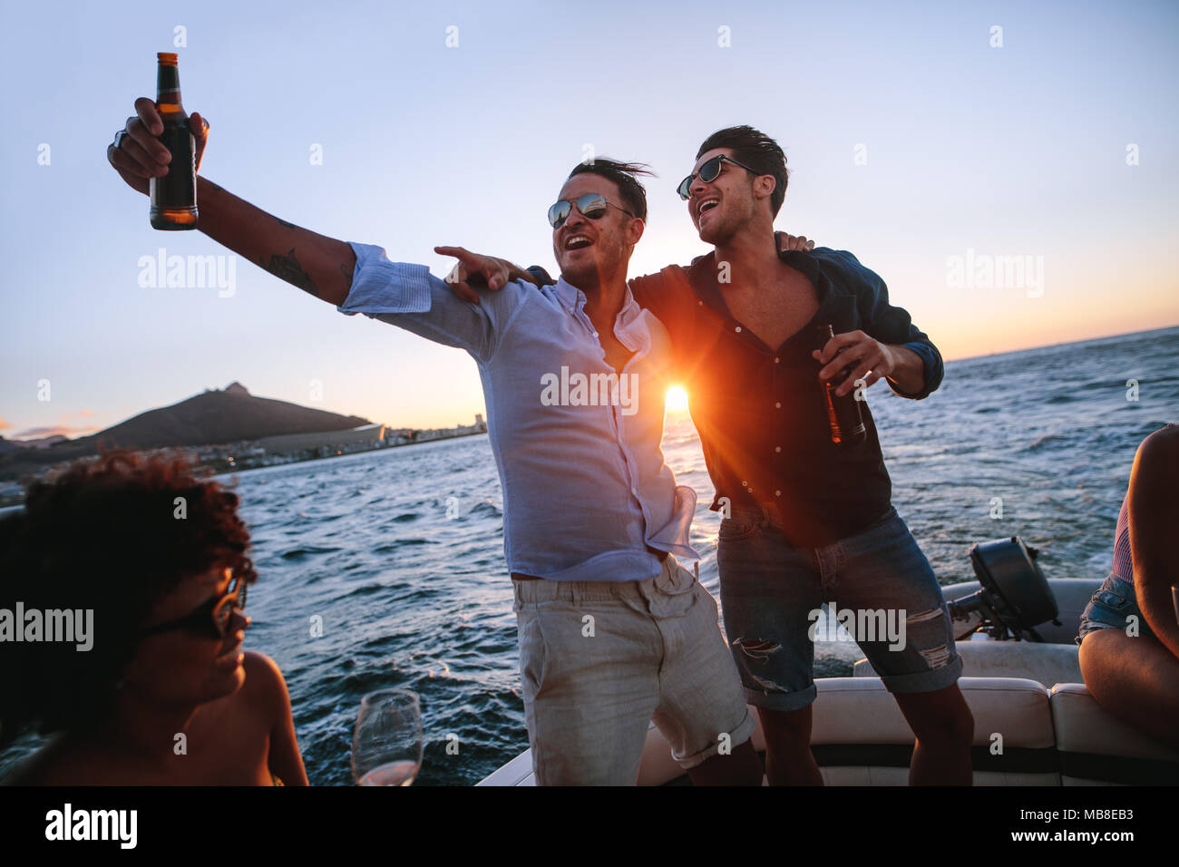 Men having a great time at boat party at sunset. Friends partying on a yacht with drinks. Stock Photo