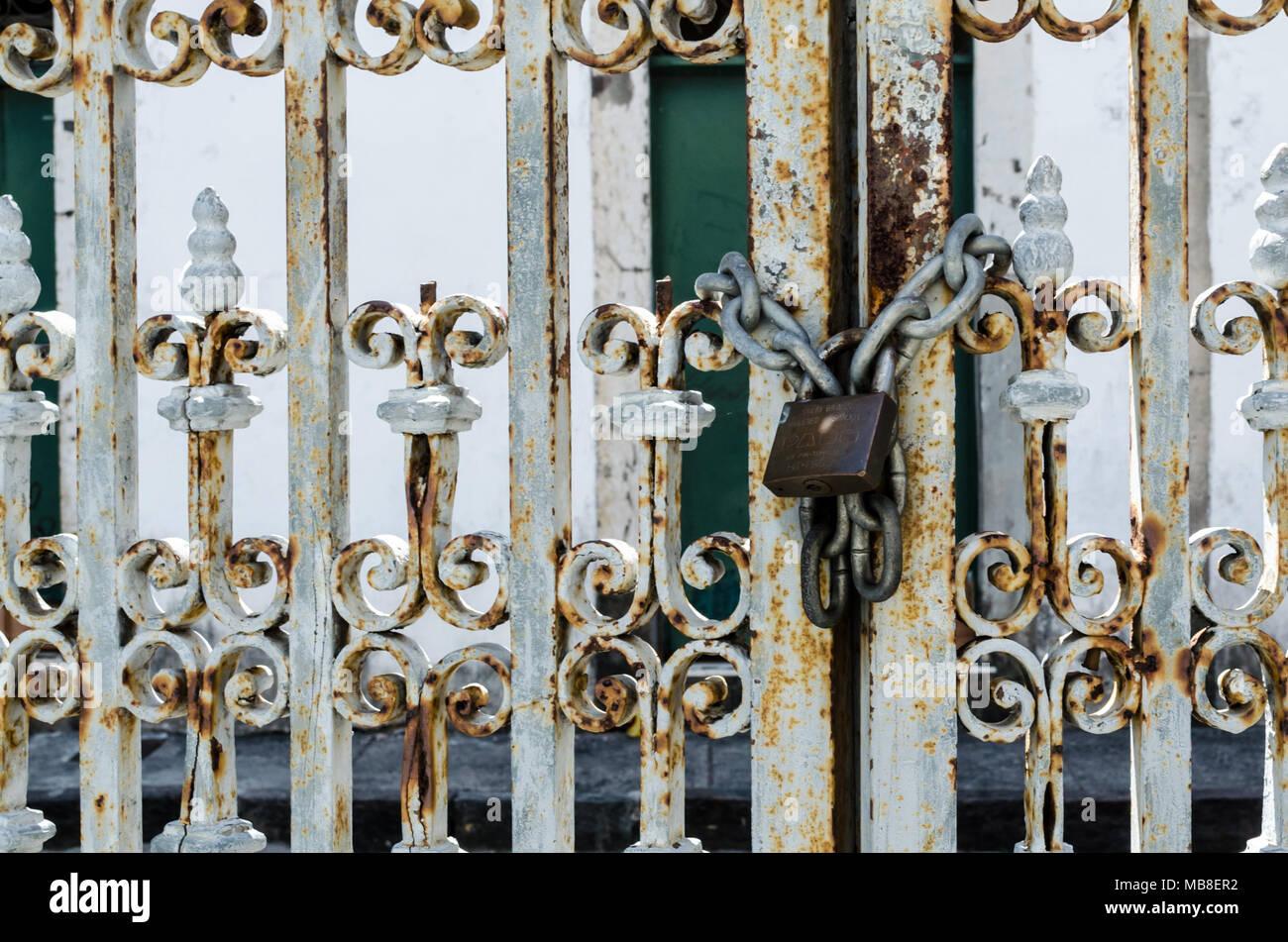 Rusty iron door with padlock attached to a chain, closing the door. Iron door worked with details. Padlock on the right. Stock Photo