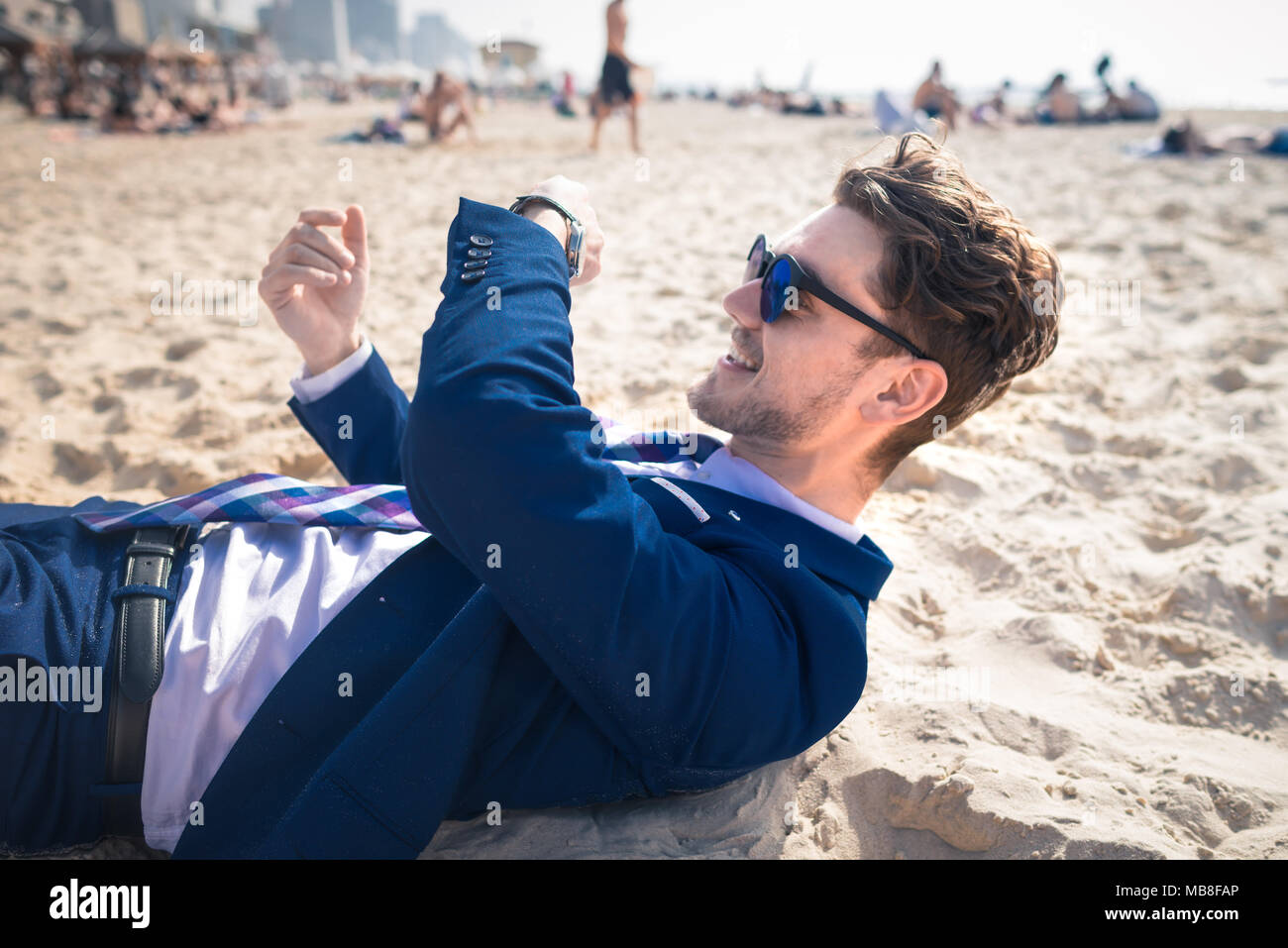 Attractive young man in elegant suit has time to rest. Funny guy relaxes on  the beach and looks on the wristwatch Stock Photo - Alamy