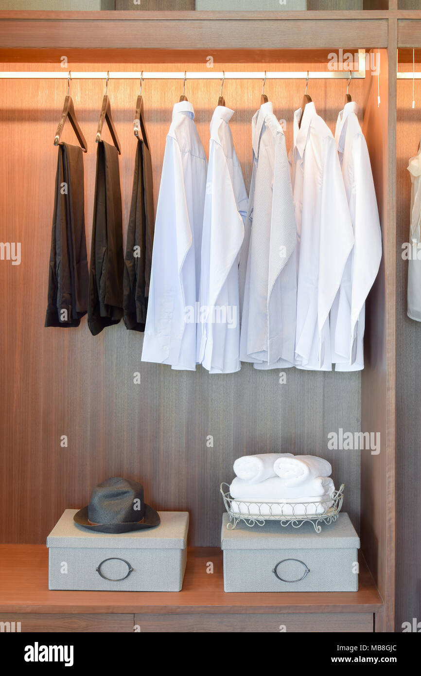 Row Of White Shirts And Black Pants Hanging In Wooden Wardrobe