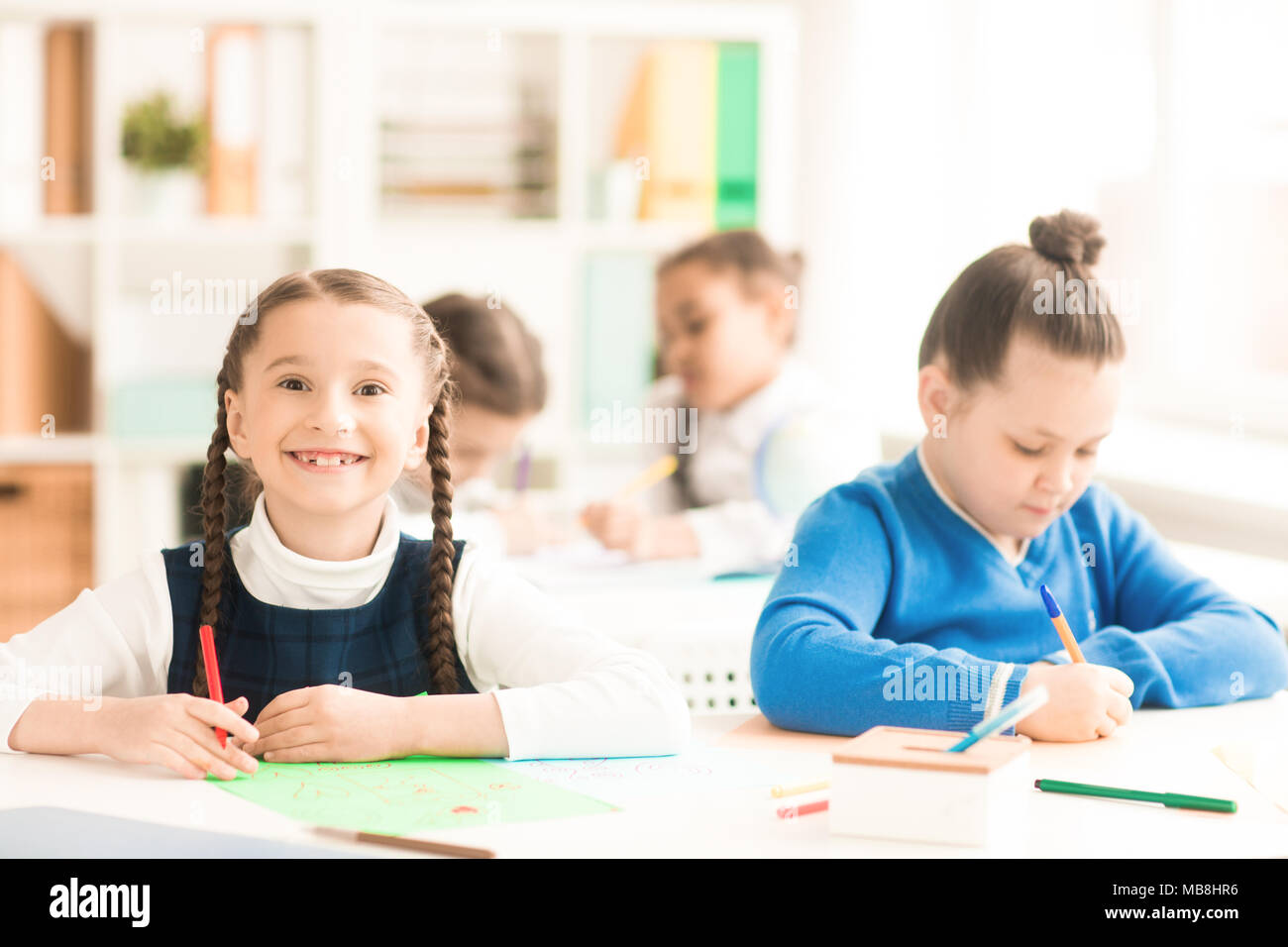 Portrait of smiling schoolgirl sitting at the desk with her classmte ...