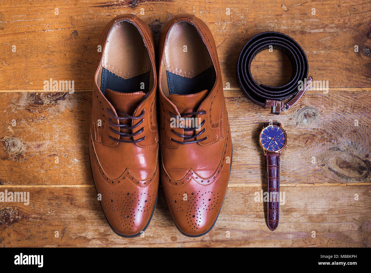 Closeup of elegant stylish brown male formal accessories isolated on brown wooden background. Top view of leather belt, shoes and watch. Preparation f Stock Photo