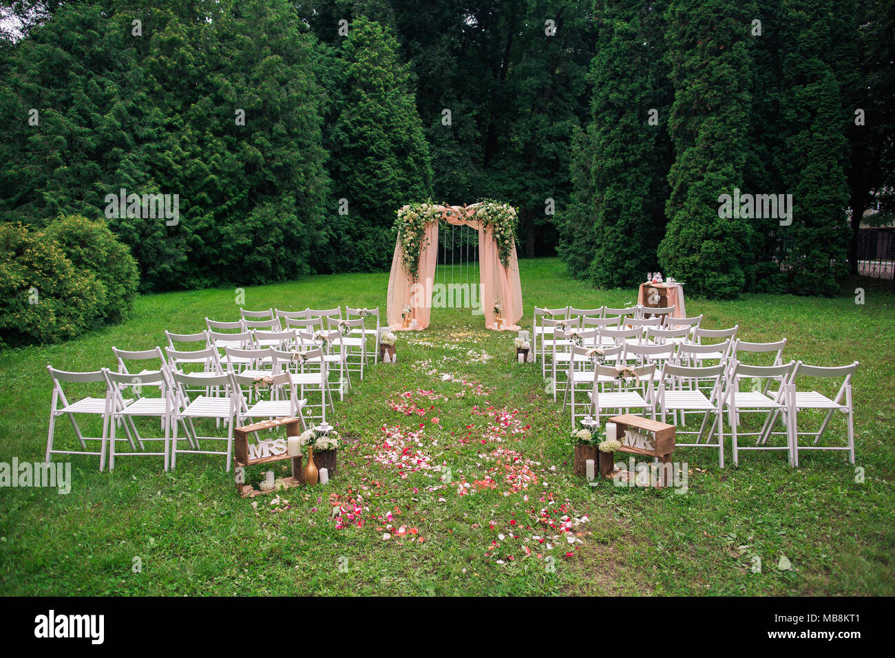 Beautiful place made with wooden square and floral roses decorations for outside wedding ceremony in green park. Rows of many empty wooden chairs read Stock Photo