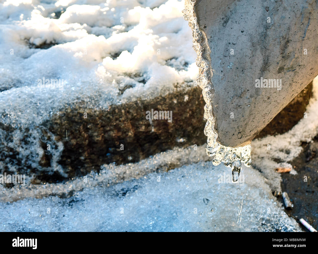 Ice and snow melting, water running down the pipe at the warm sunny