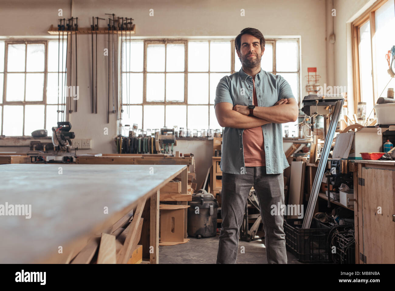 Confident young carpenter standing in his workshop full of tools Stock Photo