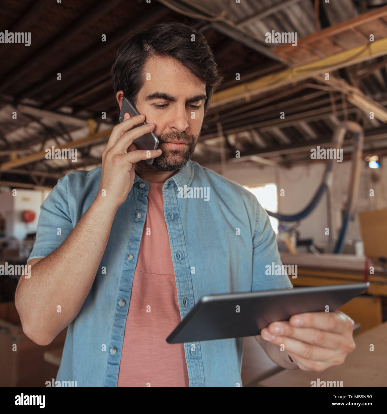 Young woodworker using a phone and tablet in his workshop Stock Photo