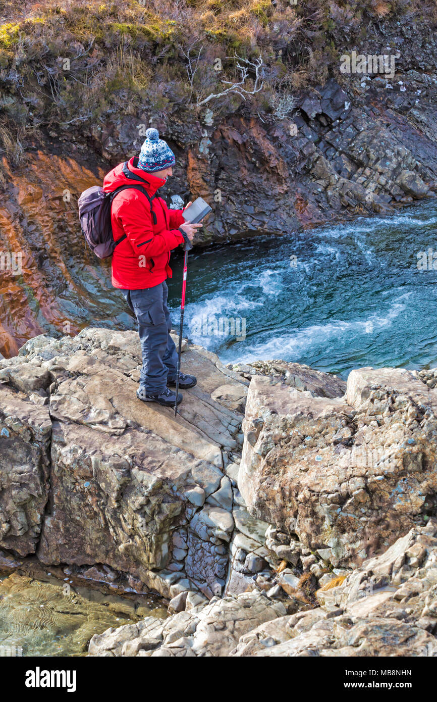 Man  holding mobile phone standing on rocks at Fairy Pools, river Brittle, Isle of Skye, Scotland, UK in March Stock Photo