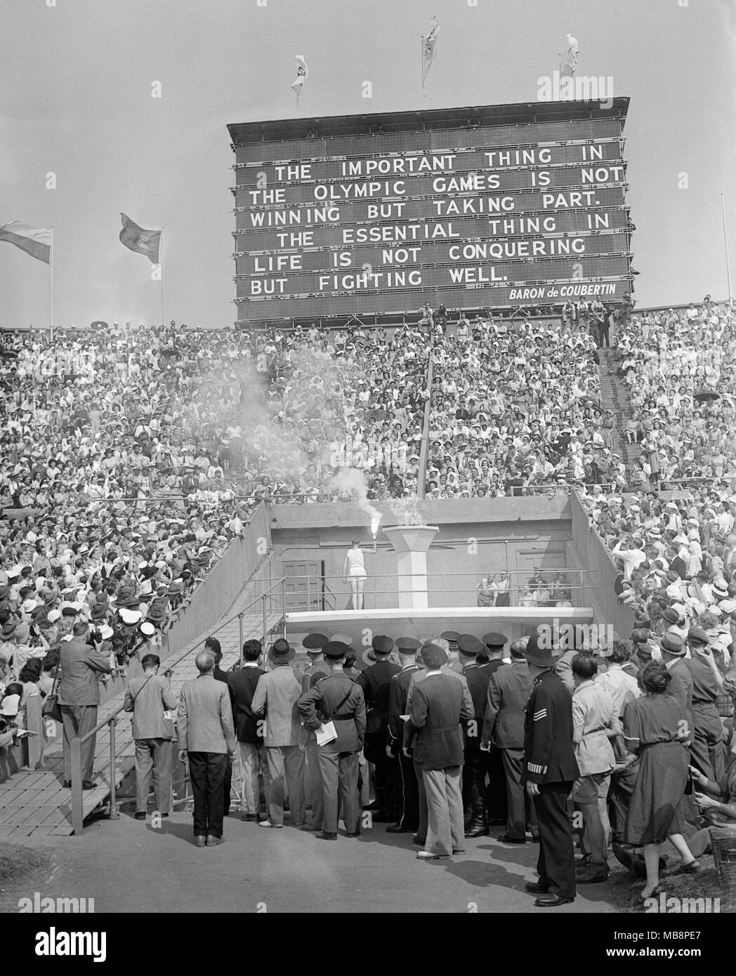 Olympic Games. London. 1948. The Olympic Flame being lit by the final torch bearer John Mark. A quote from Baron de Coubertin on the giant scoreboard behind. Stock Photo