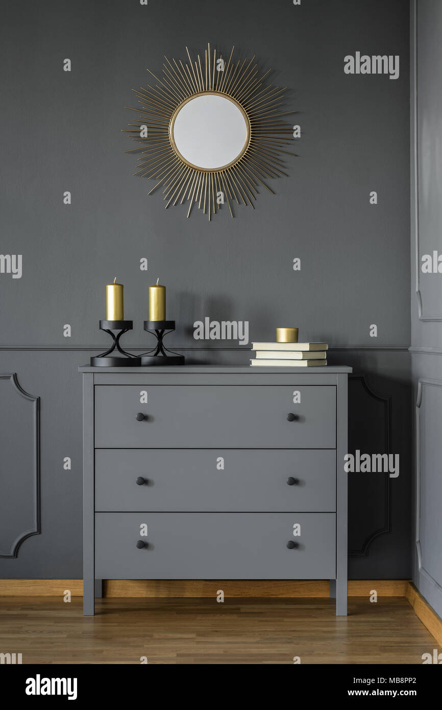 Grey cupboard with gold candles and three books standing in dark room