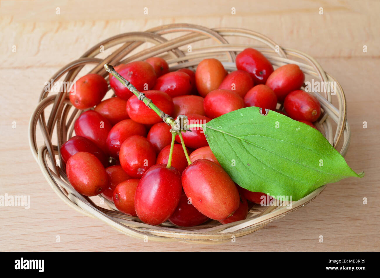 Fresh, ripe dogwood berries with green leaf in a wicker basket on wooden background, close up view Stock Photo