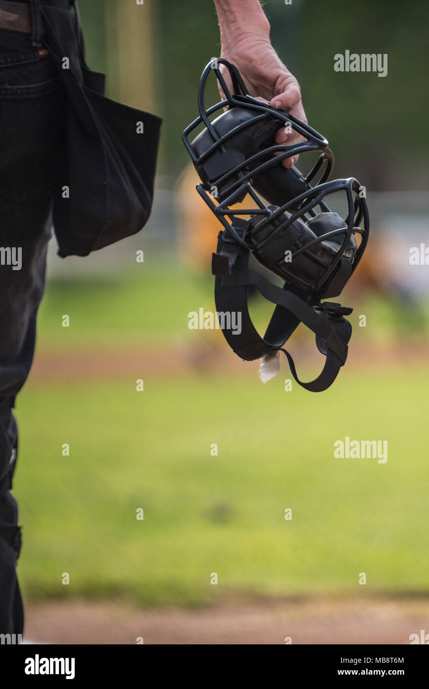 Baseball umpire holding mask in hand as he looks on the field to make a call. Stock Photo