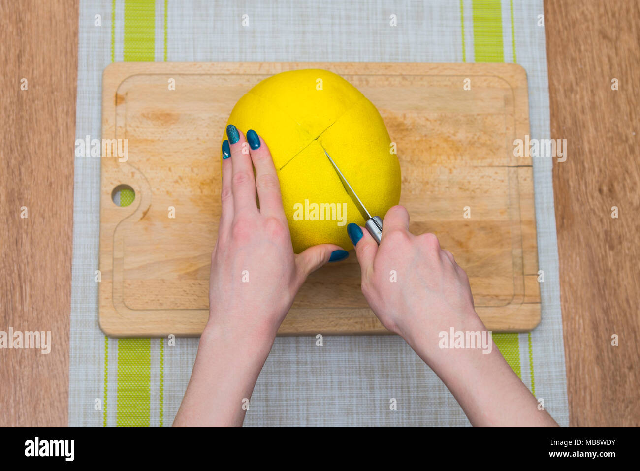 Girl cleans a pomelo on a wooden board Stock Photo