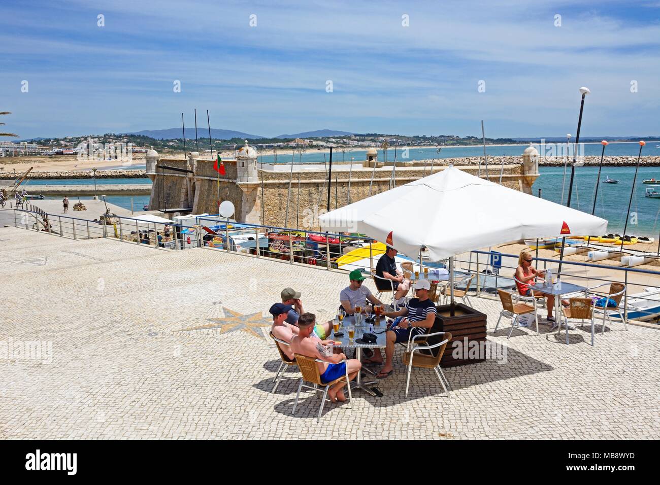 Elevated view of the Ponta da Bandeira Fort with tourists relaxing at a pavement cafe in the foreground, Lagos, Algarve, Portugal, Europe. Stock Photo