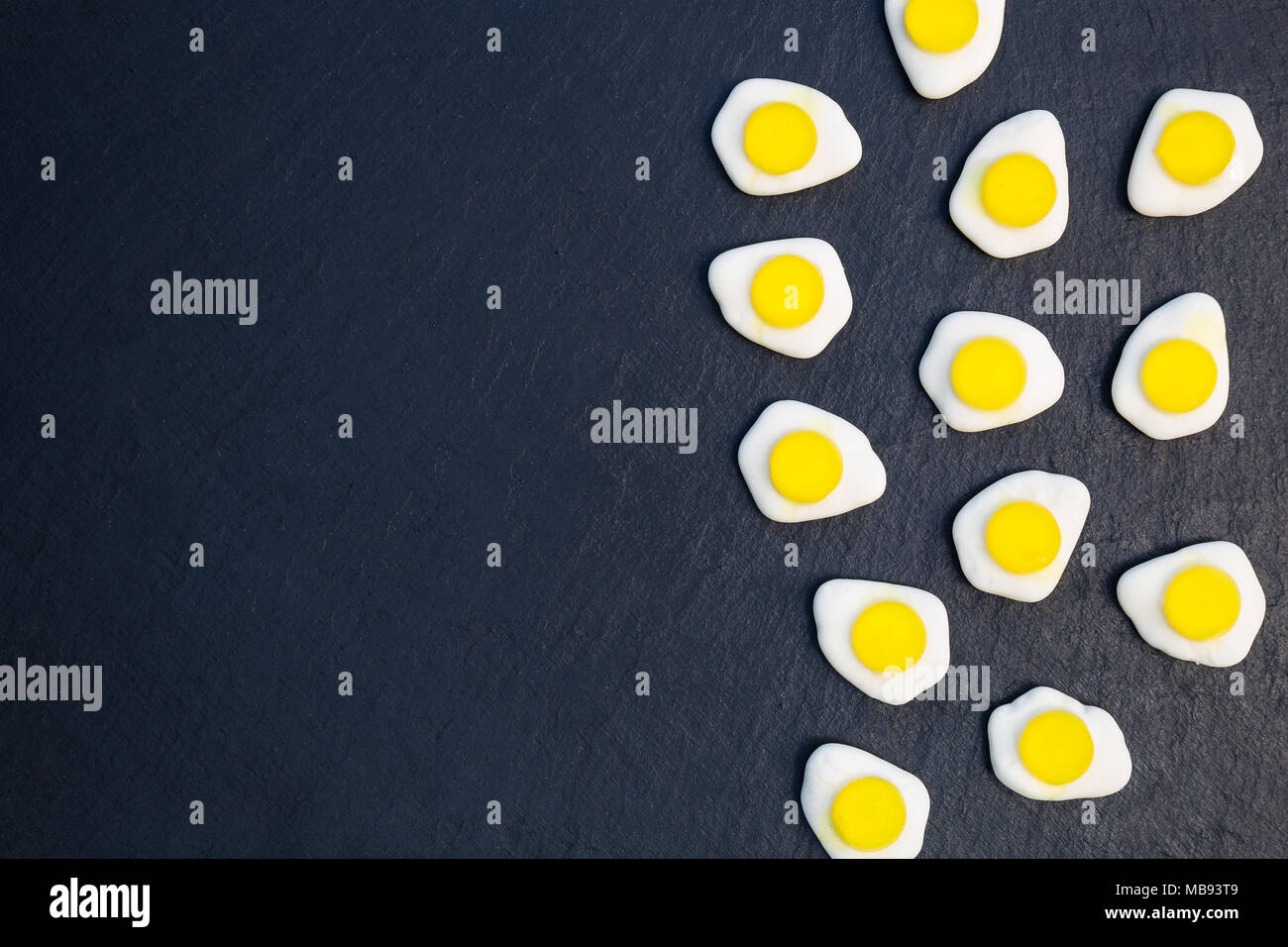 Fried eggs candy sweets overhead on dark background with copy space Stock Photo