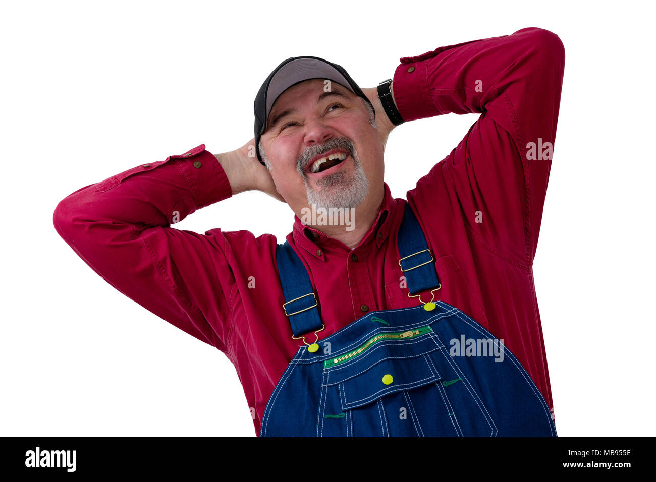 Joyful farmer or worker in bib overalls laughing in delight as he looks up with hands clasped behind his head on white Stock Photo
