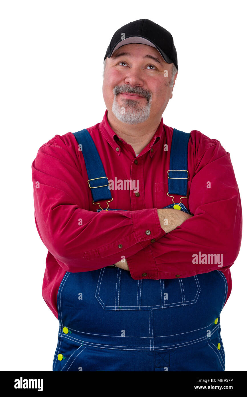 Thoughtful confident farmer or worker in dungarees standing with folded arms looking up with a pensive quiet smile as he makes his decisions isolated  Stock Photo