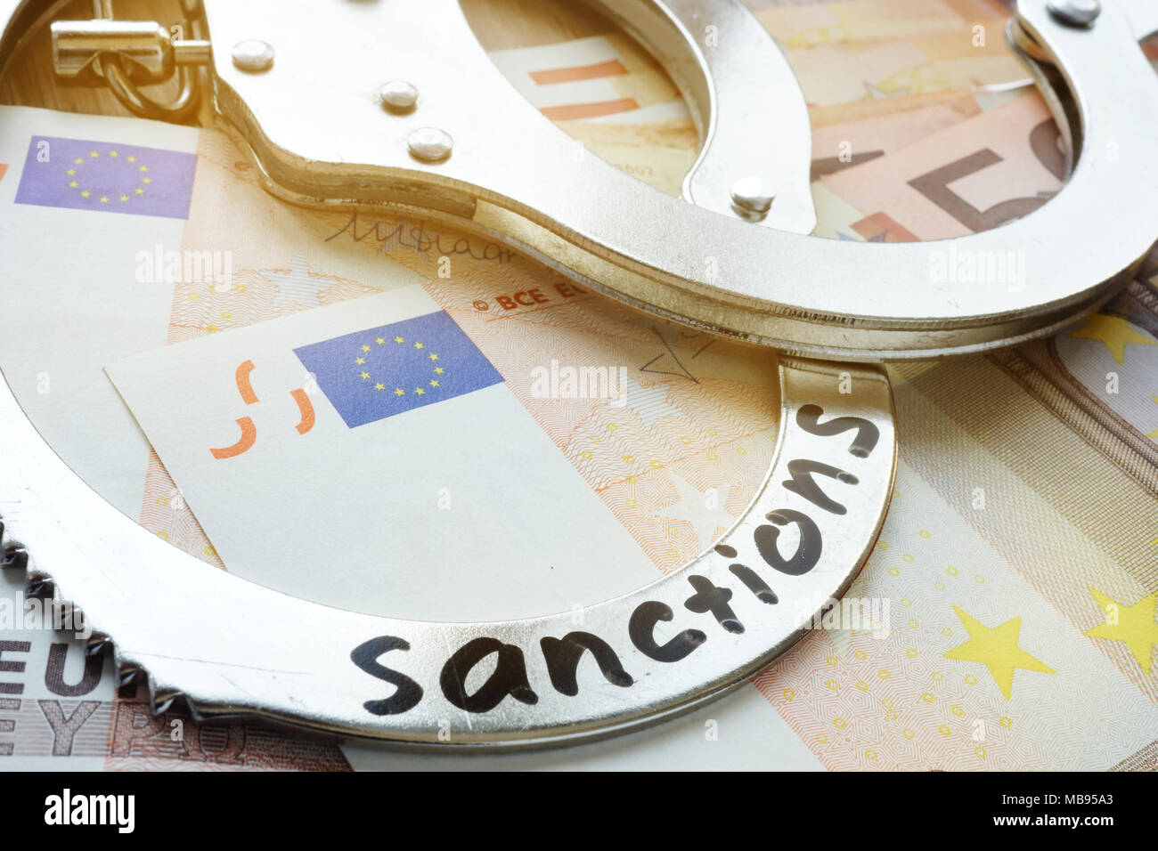 Euro bills and handcuffs with word sanctions. Economical restrictive measures. Stock Photo