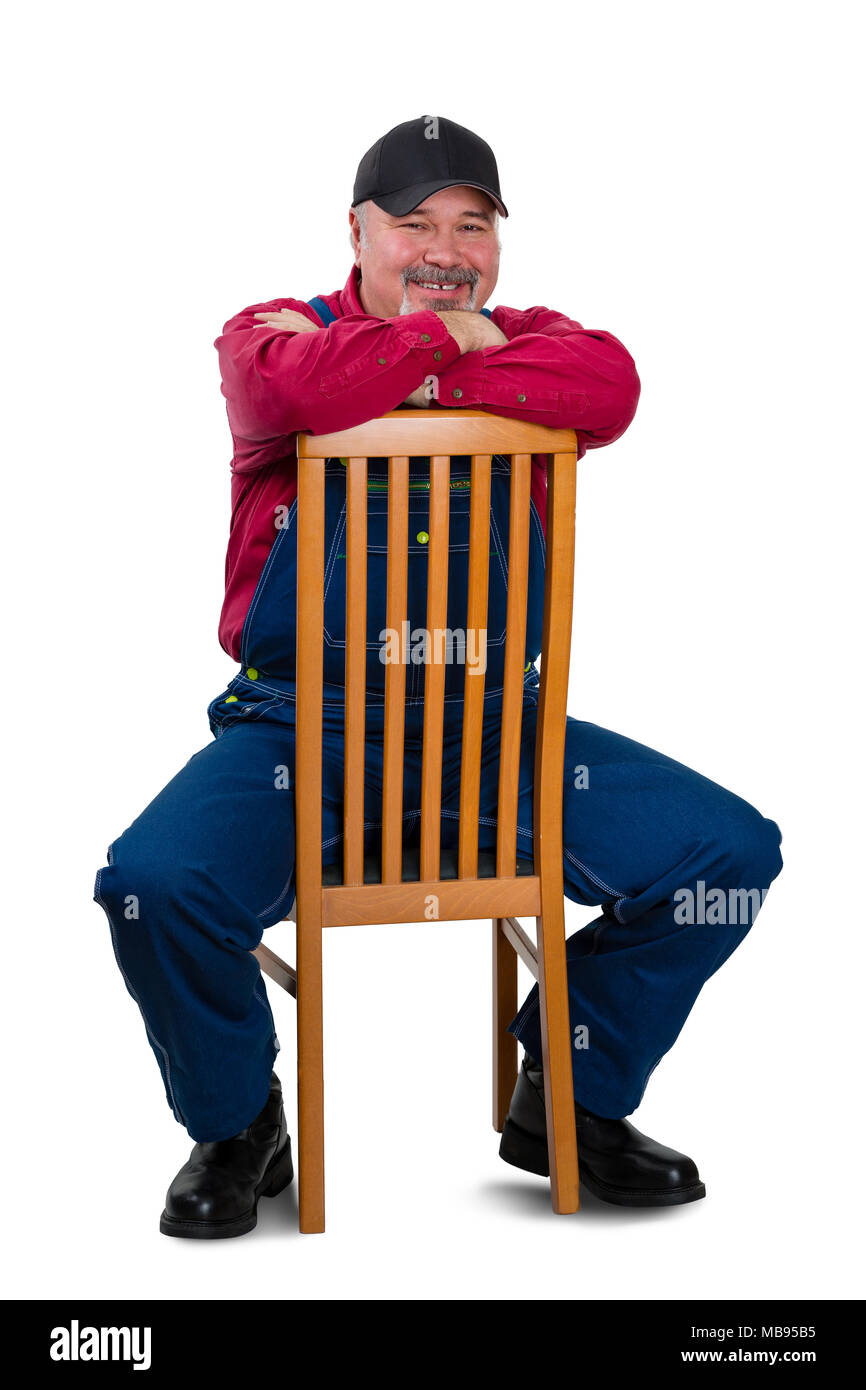 Cheerful middle class worker wearing dungarees sitting on chair against white background Stock Photo