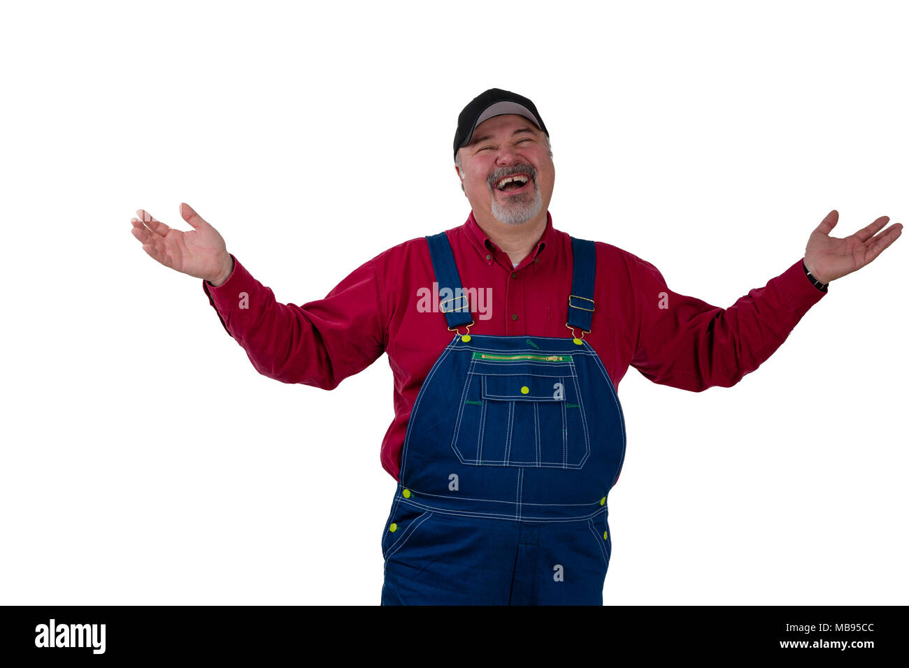 Laughing happy man in denim dungarees and a peaked cap standing raising his arms in a magnanimous gesture isolated on white Stock Photo
