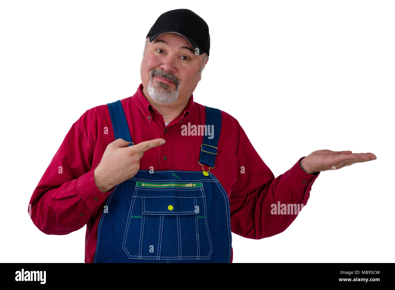 Middle-aged farmer or worker wearing a denim bi overall pointing to his empty hand over white copy space with a knowing expression of satisfaction Stock Photo
