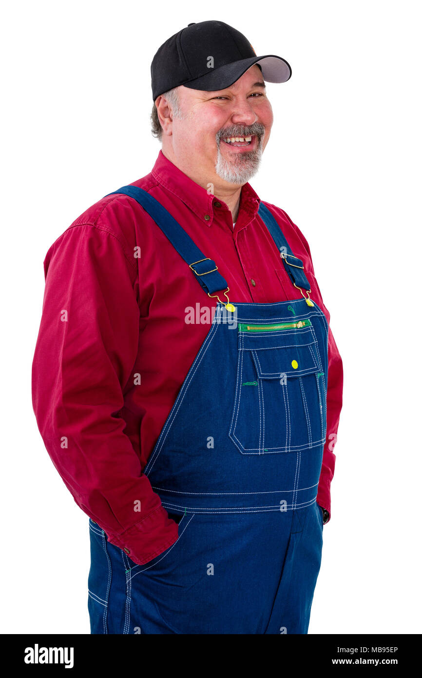 Smiling relaxed worker or farmer in overalls standing with his hands in pockets turned to the side with a look of amusement isolated on white Stock Photo