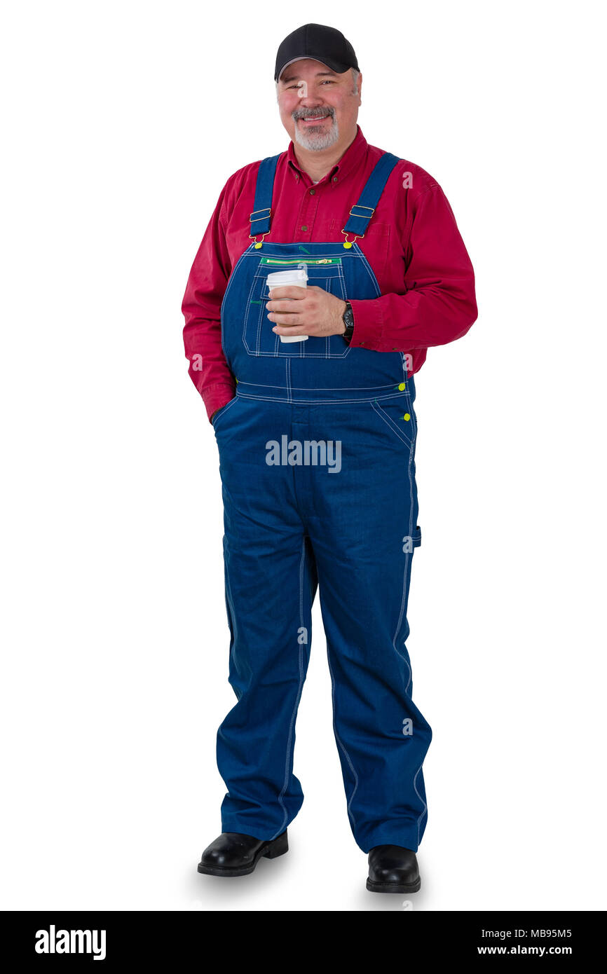 Full length portrait of a worker in denim dungarees, cap and red shirt standing smiling at the camera holding a cup of takeaway coffee isolated on whi Stock Photo