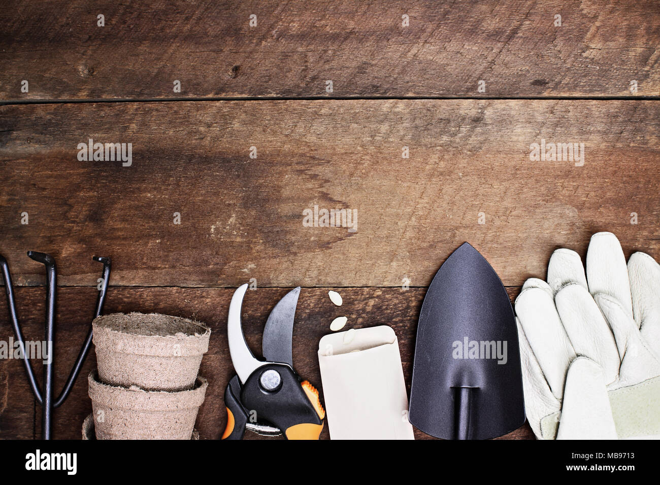 Background of various generic gardening tools, gloves and vegetable seeds shot from above over a rustic wood table in flat lay style. Stock Photo