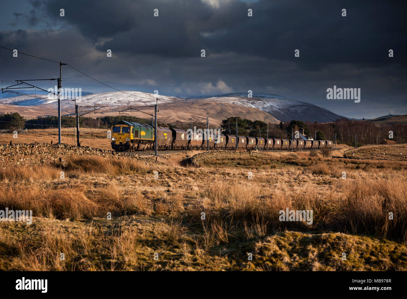 A Freightliner  class 66 locomotive passing Scout Green climbing Shap on the west coast main line with a empty merry go round coal freight train Stock Photo