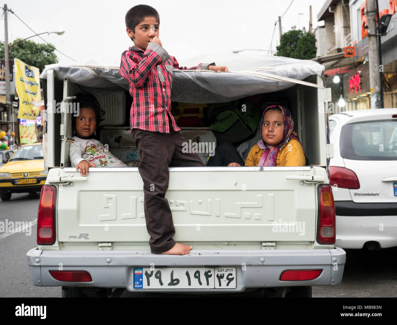 Children riding on the back of a pick-up truck in city traffic. Babolsar, Mazandaran province, Iran Stock Photo