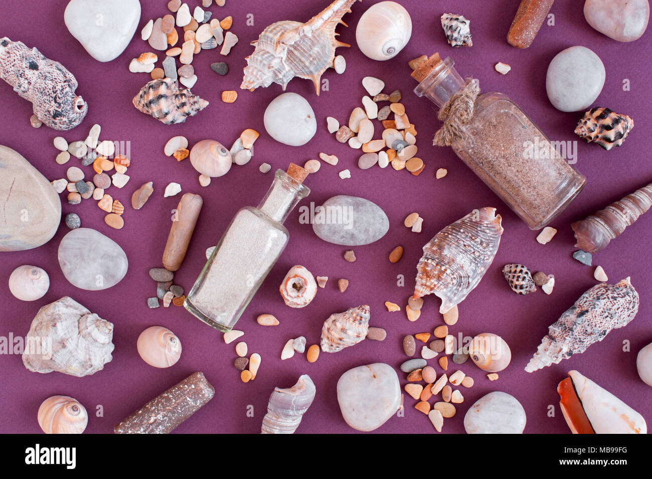 Pattern of sand in the glass bottles, sea shells and stones on the violet paper background, flat lay Stock Photo