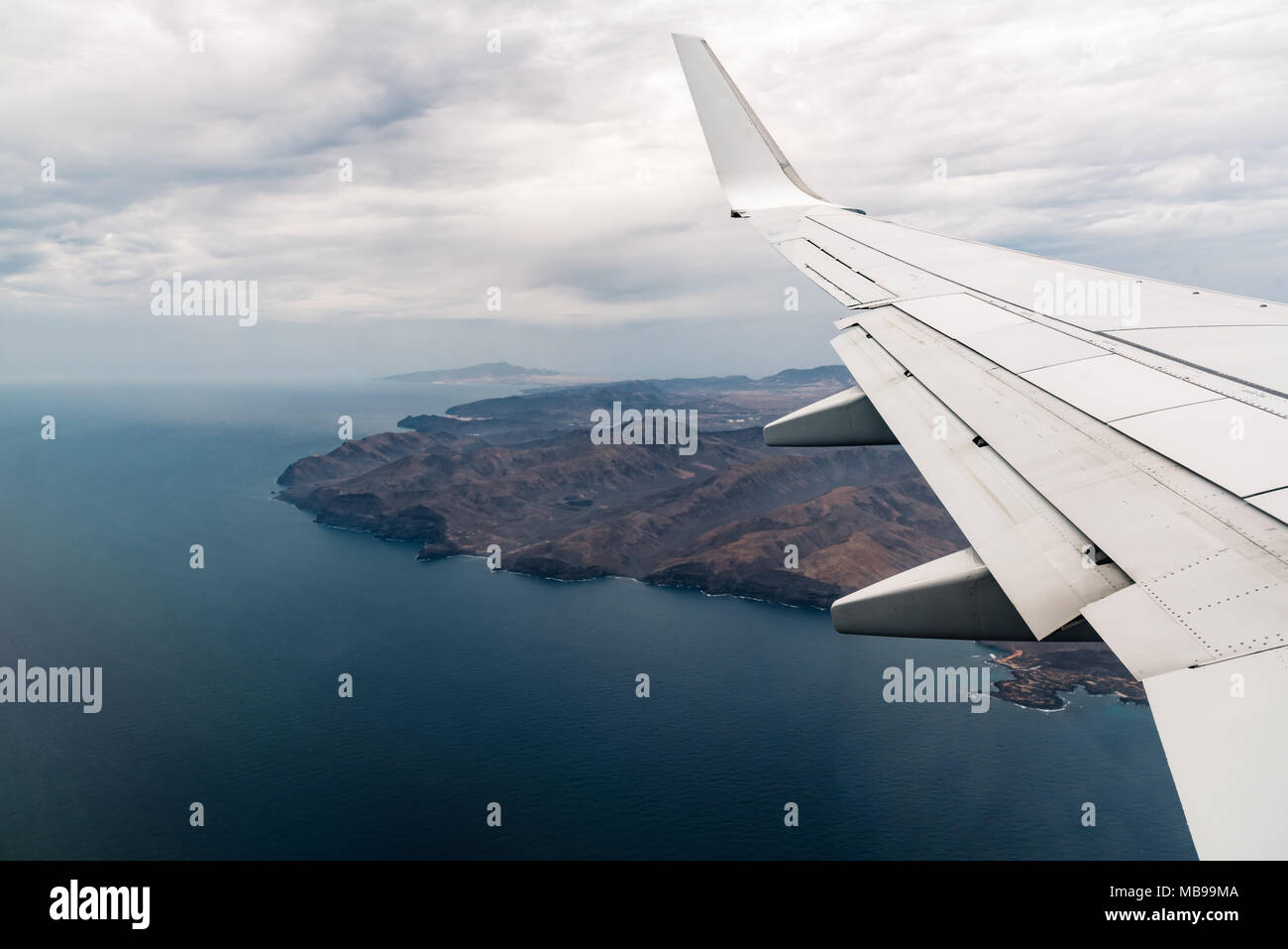 Looking through window of airplane with wing during flight against volcanic island and sea Stock Photo