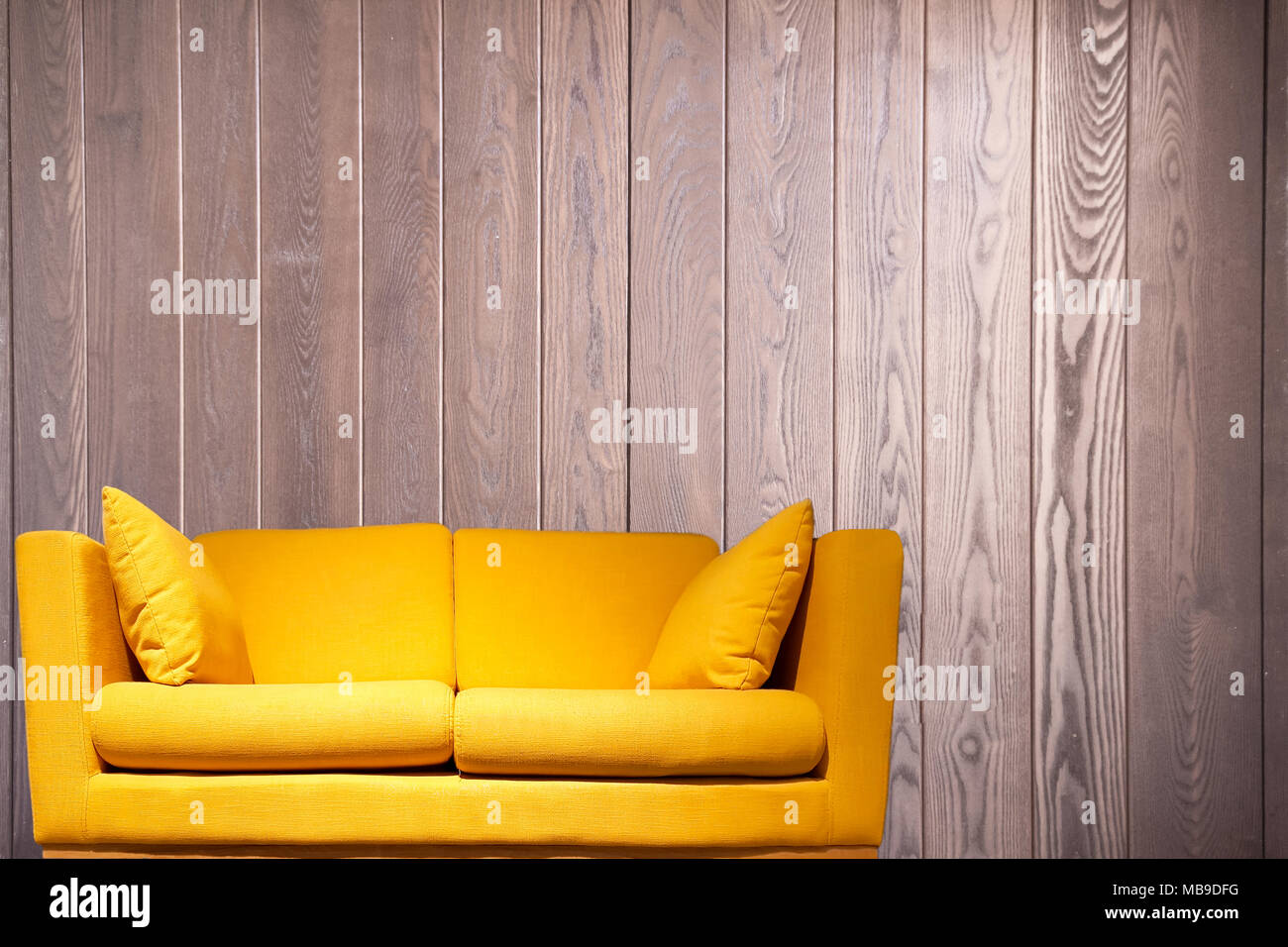 Yellow sofa in front of a wooden wall with copy space background. Stock Photo