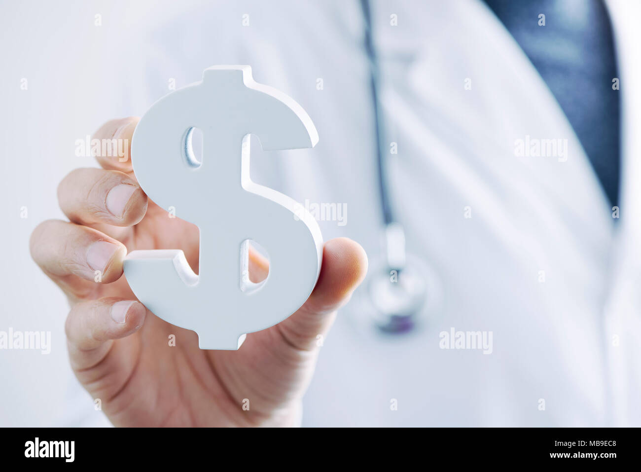 closeup of a young caucasian doctor man with a dollar symbol in his hand, depicting the concepts of the healthcare industry or the healthcare costs Stock Photo