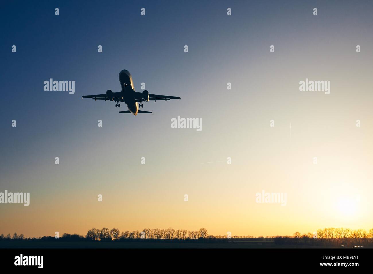 Silhouette of the airplane landing against moody sky at golden sunset. Stock Photo