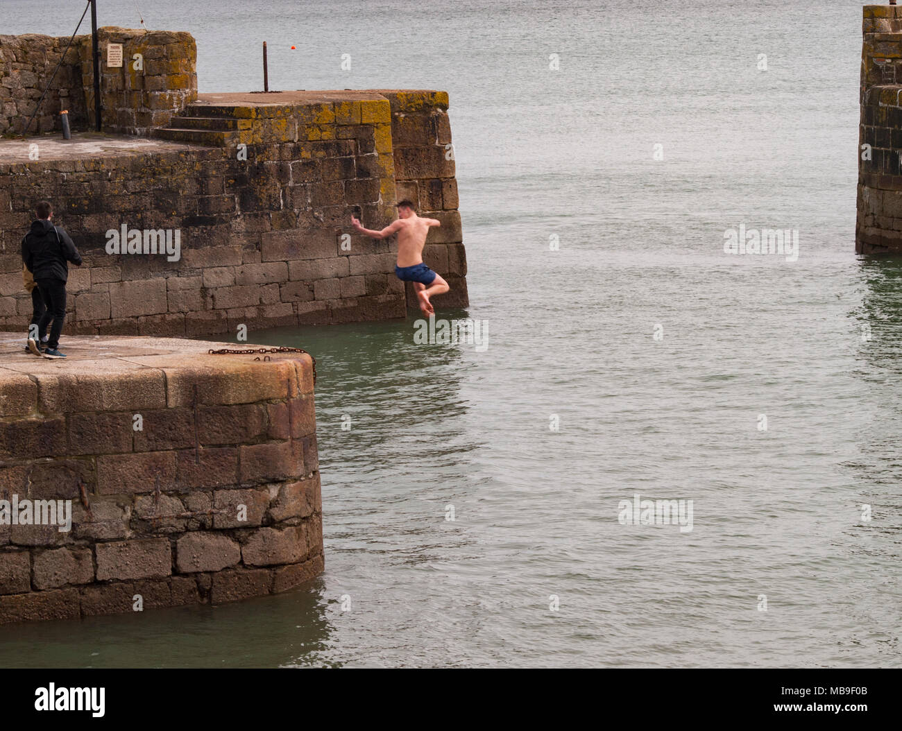 Careless and irresponsible teenagers jumping of the harbour wall into the sea in Charlestown, Cornwall. Stock Photo