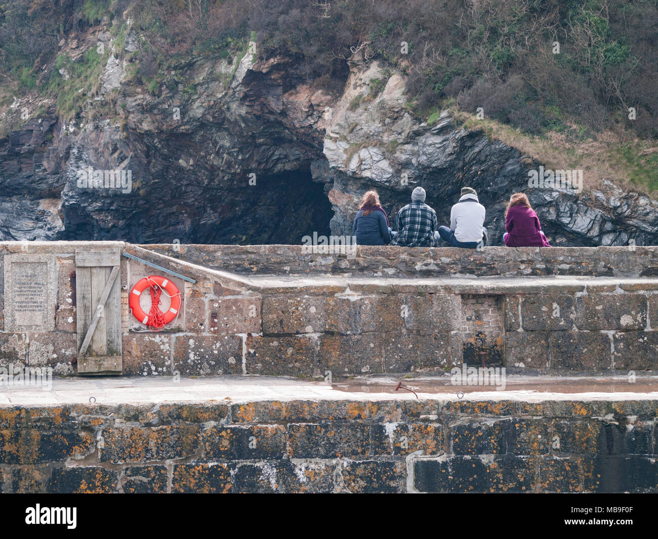Four teenagers sitting on the harbour wall in Charlestwon, Cornwall. Stock Photo