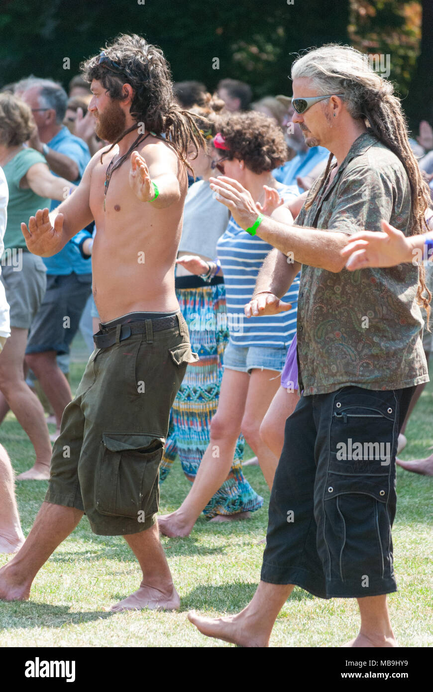 People attending an outdoor yoga class at a music festival. Men with long hair in dreadlocks. Stock Photo