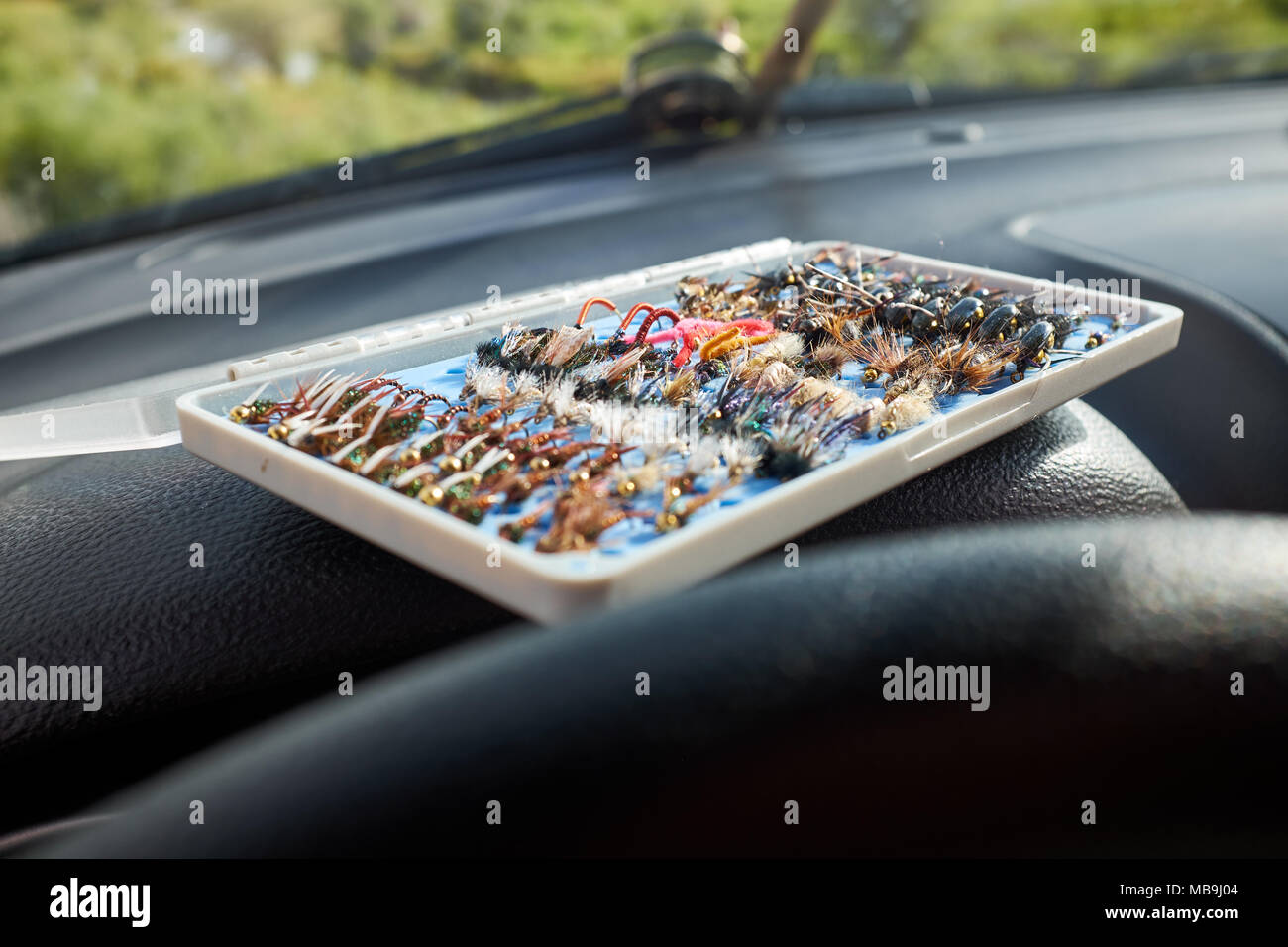 Opened box of specialist flies for fly fishing inside a car with a