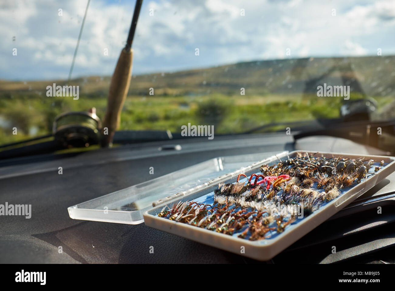 Open box of hand tied fly fishing flies inside a car with a rod