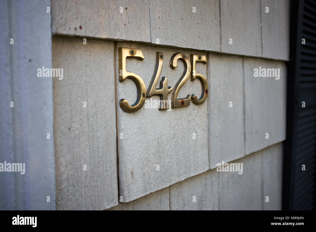 Brass number 5425 on an exterior wall mounted on the cladding identifying the property and address in an oblique angle view Stock Photo