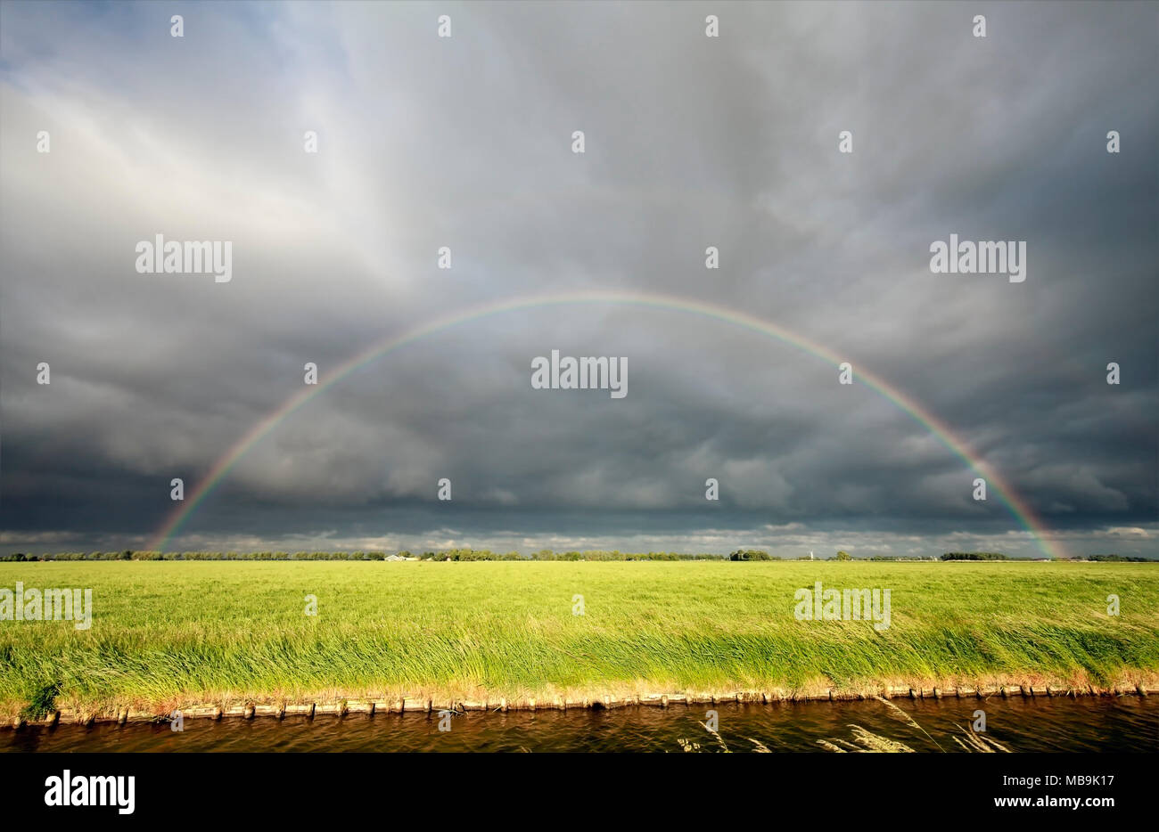rainbow over green meadow and river in countryside Stock Photo