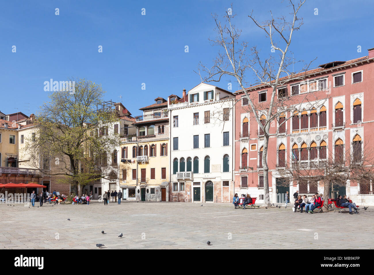 Campo San Polo, San Polo, Venice, Veneto, Italy in spring with local Venetians relaxing on benches in the sunshine under trees Stock Photo