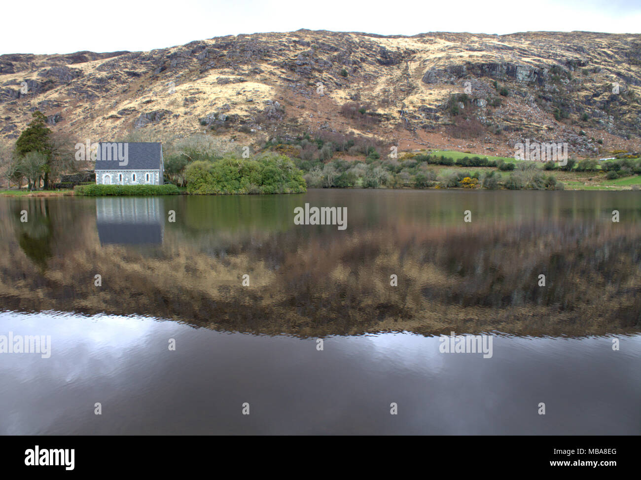 gougane barra church and  shrine of Saint Finbarr, the first bishop of cork, reflected in the atmospheric lake surrounding the church. Stock Photo