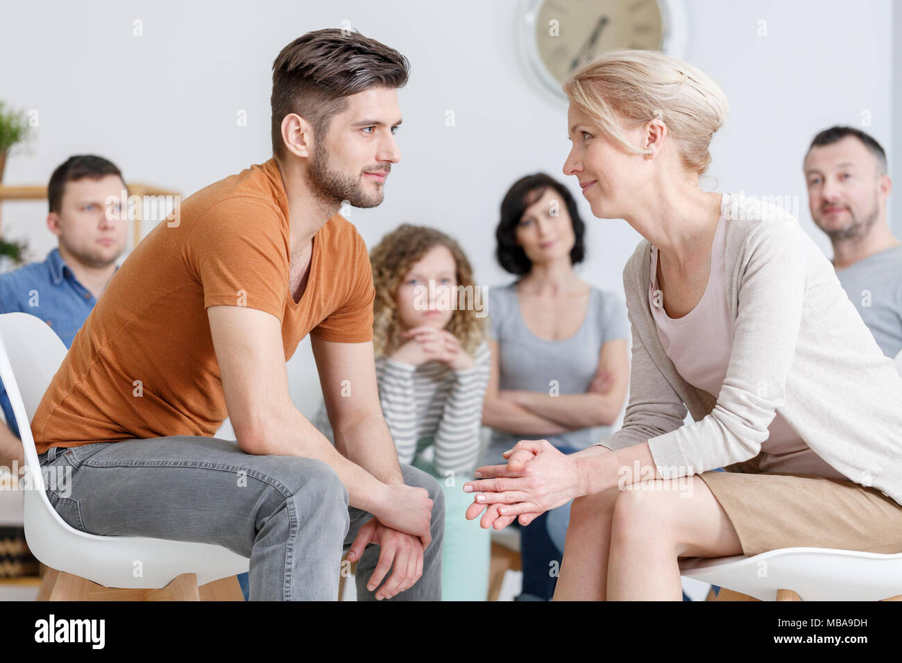 Young man and middle-aged woman sitting and looking into each other's eyes with other people in the background Stock Photo
