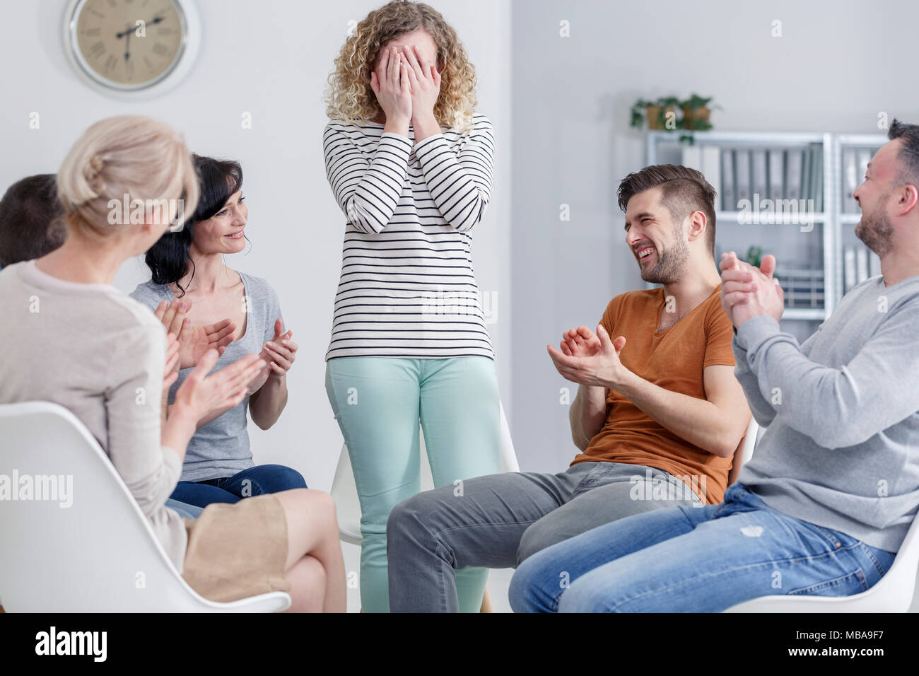 Girl hiding her face in her hands and happy people laughing and clapping in group psychotherapy Stock Photo
