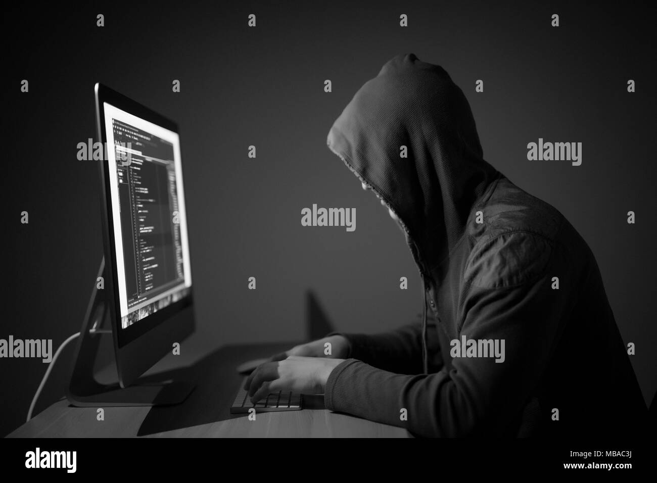 Computer hacker in hood working in dark room Stock Photo