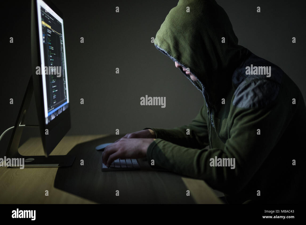 Hooded computer hacker stealing information with pc. Dark background Stock Photo