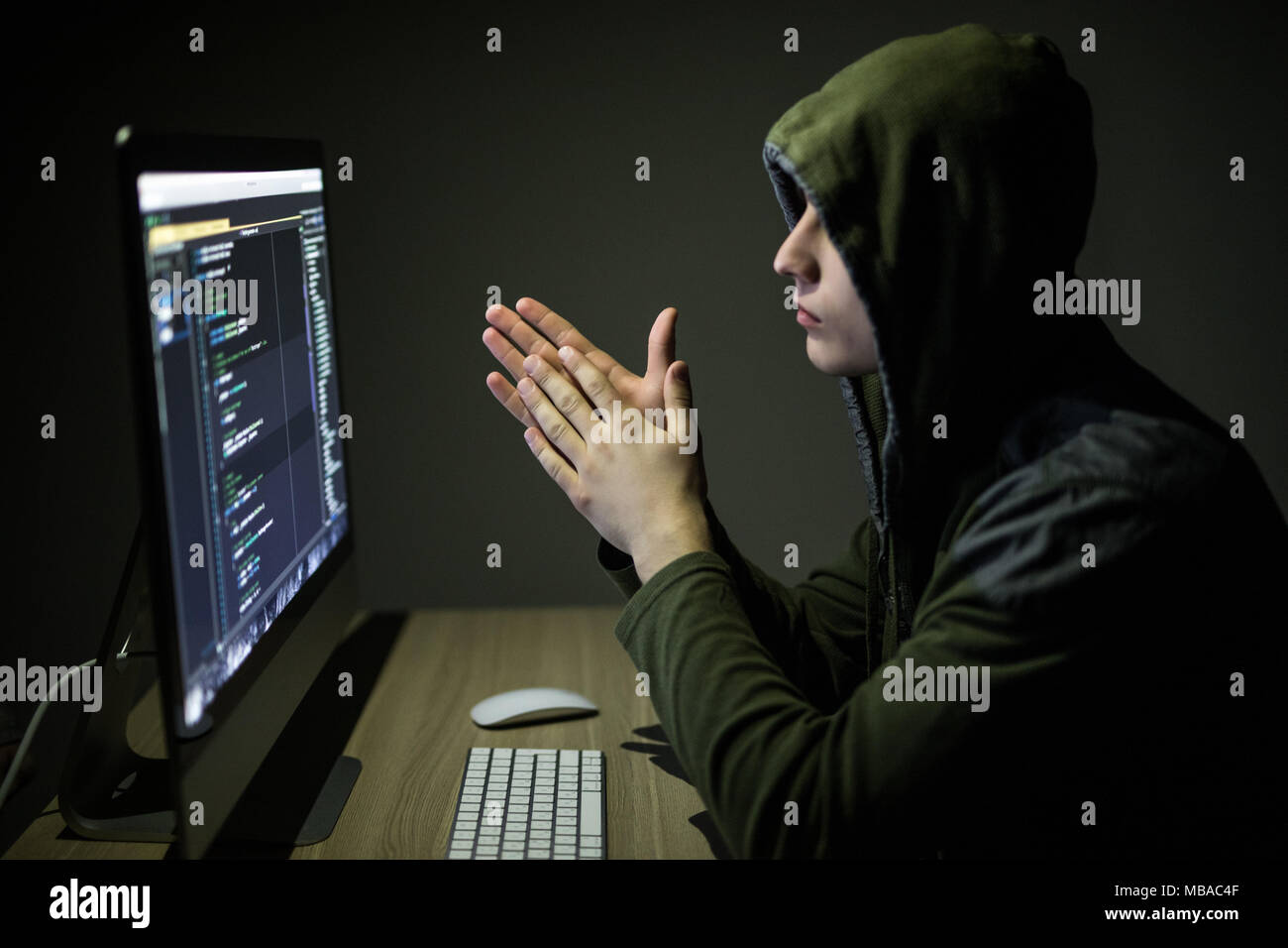 Hacker in glasses breaking code. Criminal hacker penetrating network system from his dark hacker room. Stock Photo