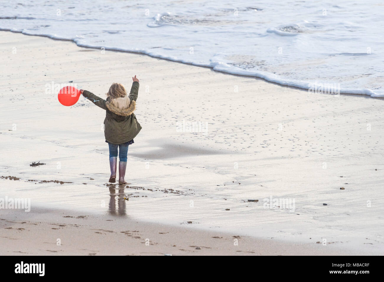 A little girl holding a red balloon and playing on the beach. Stock Photo